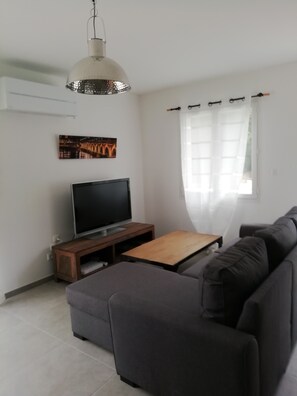 A living room with a sofa, a television on a wooden stand, a pendant light, and a window with curtains. - Cozy House - Private Hot Tub - 3 Bedrooms - Bordeaux - Sleeps 6 (les-Graves)