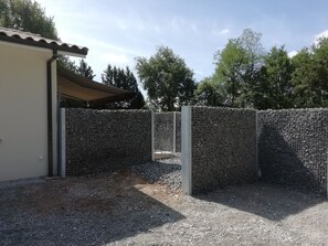 A fenced outdoor area with a gravel ground, a building with a tiled roof, and trees in the background. - Cozy House - Private Hot Tub - 3 Bedrooms - Bordeaux - Sleeps 6 (les-Graves)