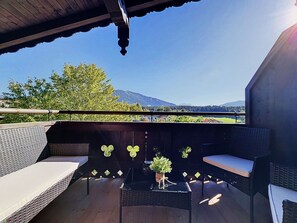 An outdoor seating area with wicker furniture and a small table, overlooking a scenic landscape with trees and mountains.
