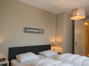 Ein Hotelzimmer mit einem Bett, einem Nachttisch mit einer Uhr, einem Wandschild mit der Aufschrift 'HAPPINESS' und einer Hängelampe.