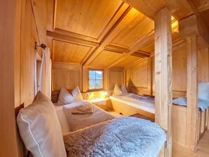 Um quarto de cabana acolhedor, com paredes e teto de madeira, duas camas, uma janela e uma pequena escrivaninha.