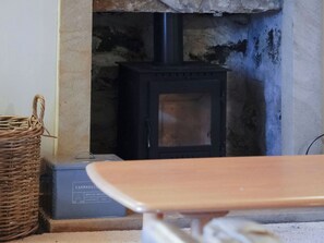Ein schwarzer Kaminofen aus Holz in einem Stein-Kamin, ein Korbwäscher und eine blaue Kiste mit dem Aufdruck 'Farmhouse Essentials'.
