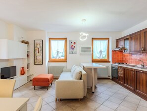 Ein modernes Wohnzimmer mit einer Couch, einem Hocker und einem Fernseher. Es gibt eine Küchenzeile mit Holdekor und einem Herd.