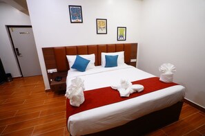 Una habitación de hotel con una cama grande, cabecera de madera, manta roja y dos almohadas.