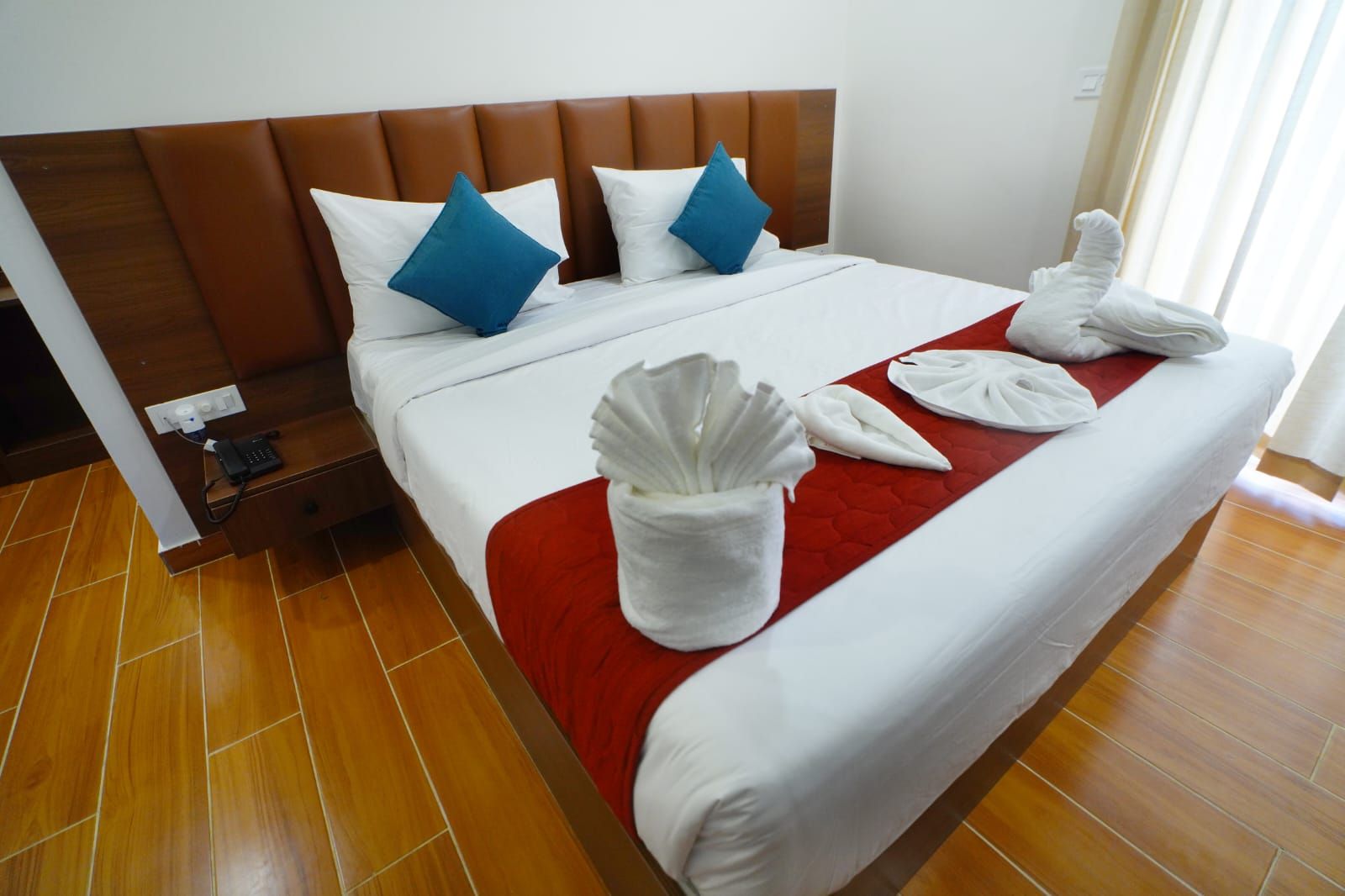 A hotel room with a large bed, a wooden headboard, and a red accent pillow.