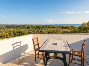 Eine Terrasse mit Tisch und Stühlen mit Blick auf eine Landschaft mit Bäumen und eine entfernte Meeransicht.