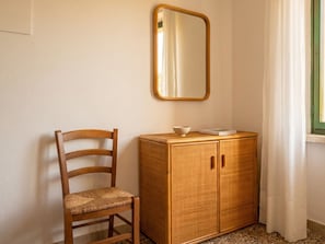 Ein Zimmer mit einem Holzhocker, einem Korbschrank und einem Spiegel an der Wand.