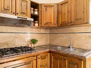 Eine Küche mit Holzausstattung, einem Edelstahlspülbecken, einem Gasherd und Marmorfliesen.