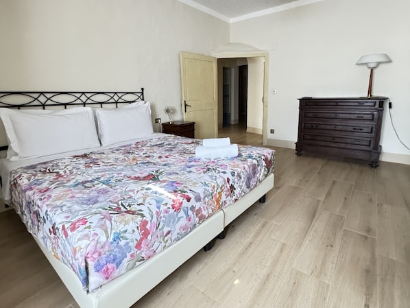 Quarto com cama, penteadeira e porta que dá para outro cômodo.