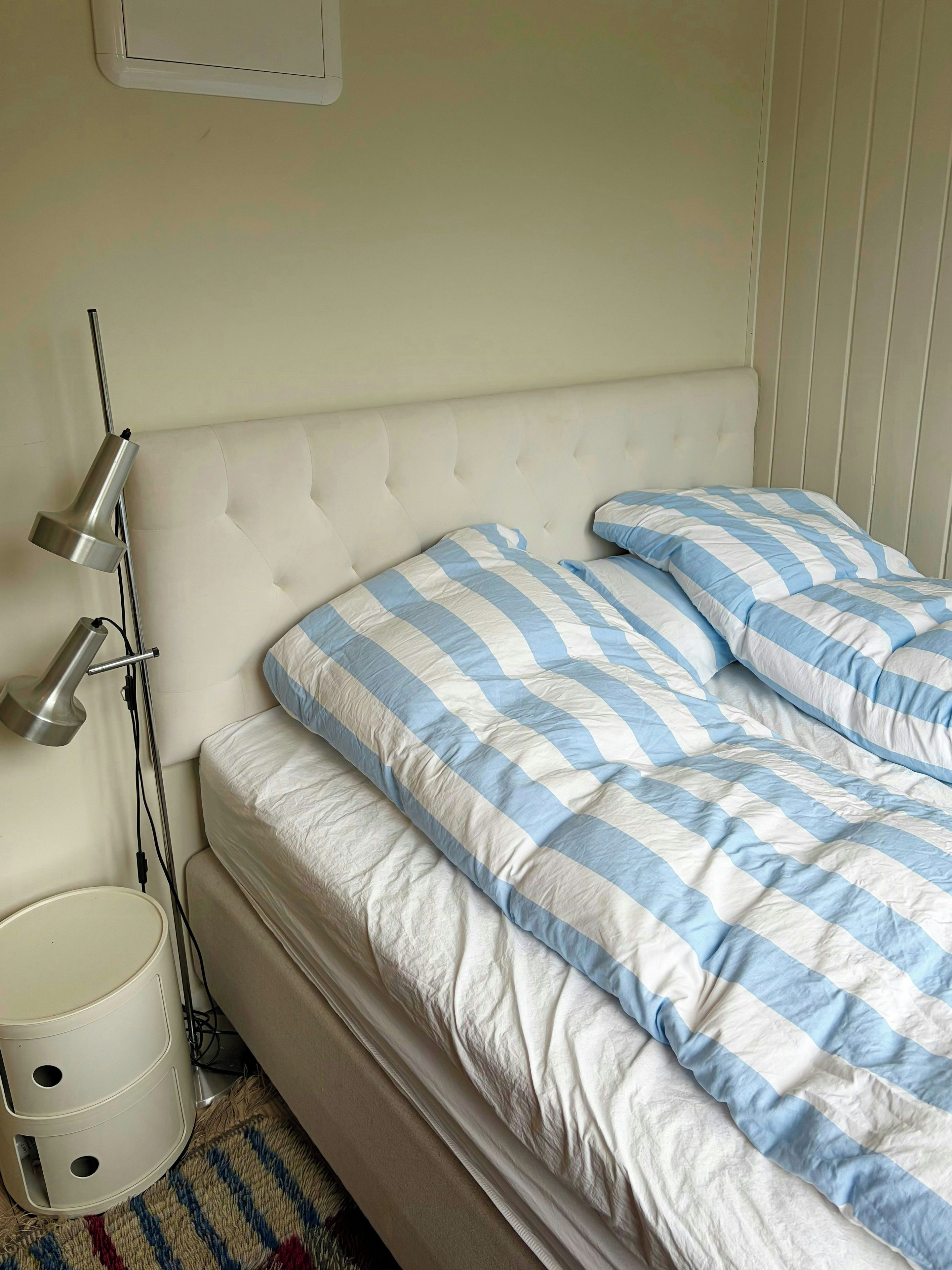 A bed with a striped bedspread, a bedside lamp, and a white bedside table with a lamp.