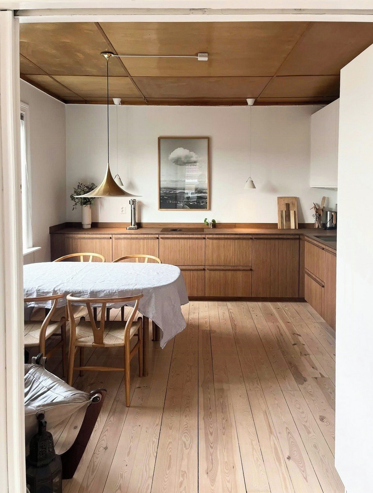 Un comedor con una mesa redonda y sillas, armarios de madera, una lámpara colgante y un cuadro en la pared.