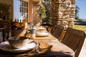 A wooden dining table set with plates, bowls, and a bottle, surrounded by chairs. - Villa La Roche d’Or | Panoramic Pool (Tourrettes-sur-Loup)