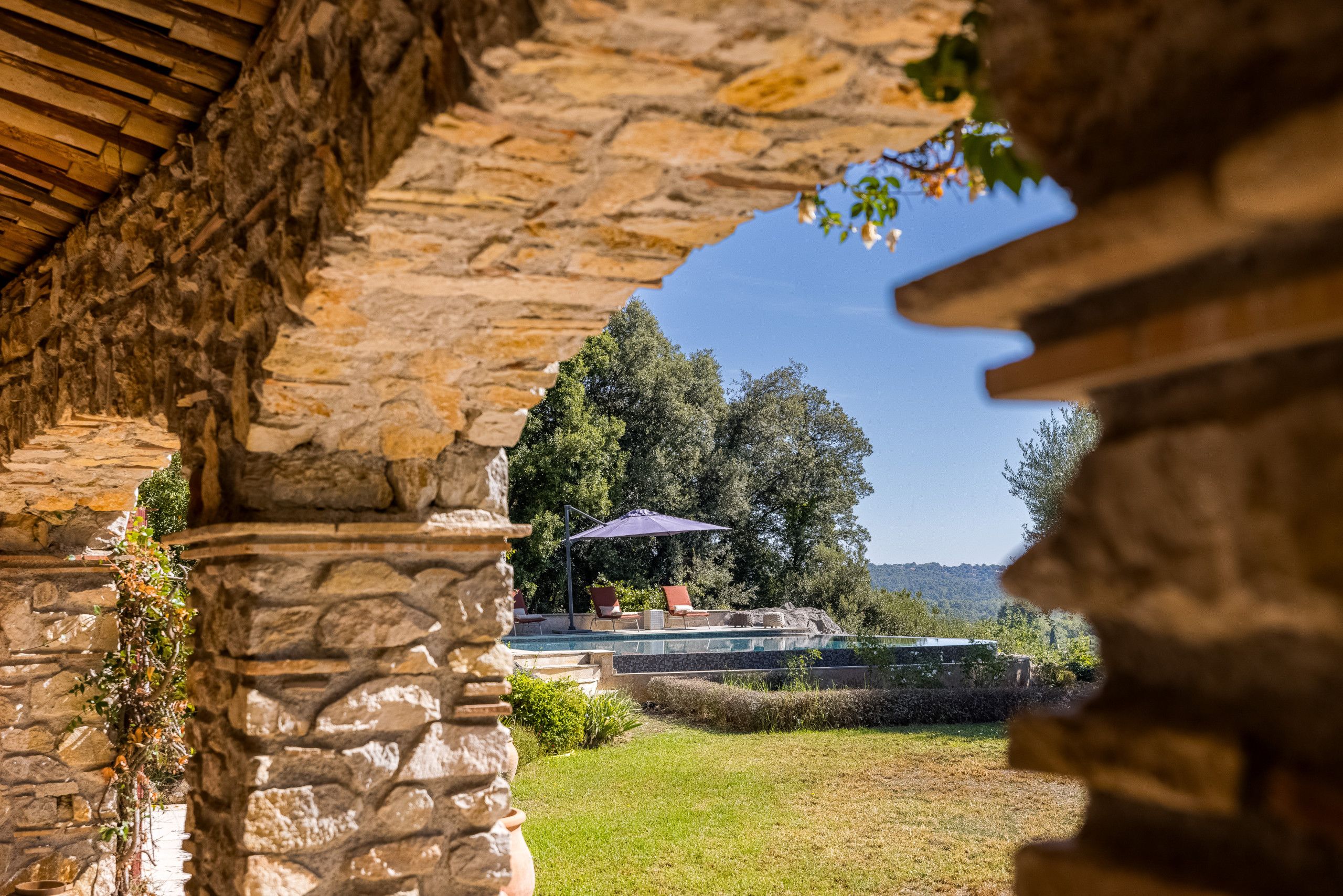 An outdoor swimming pool area with stone walls and a view of trees and hills.