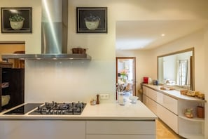 A modern kitchen with a gas stove, stainless steel range hood, and a large window. - Villa La Roche d’Or | Panoramic Pool (Tourrettes-sur-Loup)