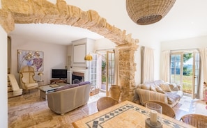A spacious living room with a stone archway, a fireplace, and a view of the outdoors. - Villa La Roche d’Or | Panoramic Pool (Tourrettes-sur-Loup)