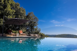 An infinity pool with clear blue water, surrounded by lounge chairs and an umbrella. - Villa La Roche d’Or | Panoramic Pool (Tourrettes-sur-Loup)