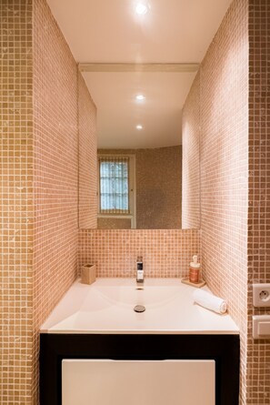 Un baño con pared de azulejos, un lavamanos, un espejo y una ventana.