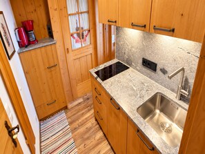 Eine kleine Küche mit Holzausstattung, einem Edelstahlspülbecken und einer schwarzen Induktionskochplatte.