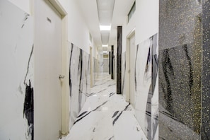 Un couloir aux murs blancs, doté de sols en marbre noir et blanc et de portes ornées de motifs noir et blanc.
