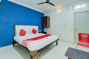 Une chambre d’hôtel avec un lit, une table de chevet, une chaise rouge et une armoire.