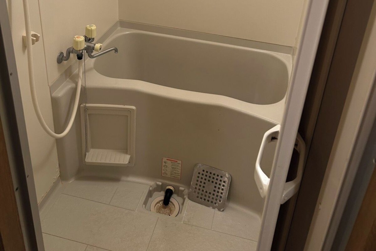 Een compacte, afgesloten badkamer met een badkuip, een douchekop en een vloerafvoer.