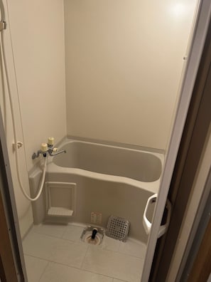Een compacte, afgesloten badkamer met een badkuip, een douchekop en een vloerafvoer.