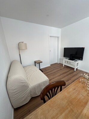 A minimalist living room with a sofa, a television on a white stand, a small table, and a lamp. - Rental: Doktorberg 20.5 (Berchtesgaden)