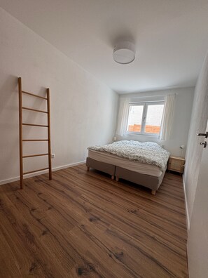 A bedroom with a wooden floor, a bed with a patterned bedspread, a window with curtains, and a wooden ladder. - Doktorberg Vacation Rental 20.5 (Berchtesgaden)