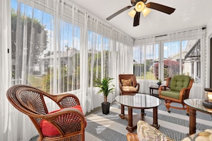 A sunroom with large windows, wicker furniture, and a ceiling fan. - Golfer's Lounge - 3/2 w/ 4-Seat Golf Cart in The Villages - De Le Vista (De La Vista, The Villages)