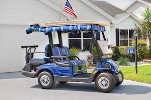 A golf cart parked in front of a house with a garage. - Golfer's Lounge - 3/2 w/ 4-Seat Golf Cart in The Villages - De Le Vista (De La Vista, The Villages)