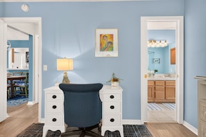 A room with a blue wall, a white dresser with drawers, a chair, a lamp, and a painting. - Golfer's Lounge - 3/2 w/ 4-Seat Golf Cart in The Villages - De Le Vista (De La Vista, The Villages)