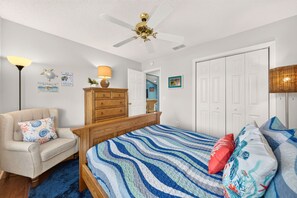 A bedroom with a bed, a chair, a dresser, a ceiling fan, and a door. - Golfer's Lounge - 3/2 w/ 4-Seat Golf Cart in The Villages - De Le Vista (De La Vista, The Villages)