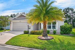 Ein bungalow mit Garage, einem gepflegten Rasen und einer Palme im Vorgarten.