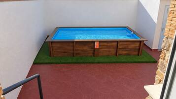 A swimming pool with a wooden deck, a red tiled floor, and a small grassy area.