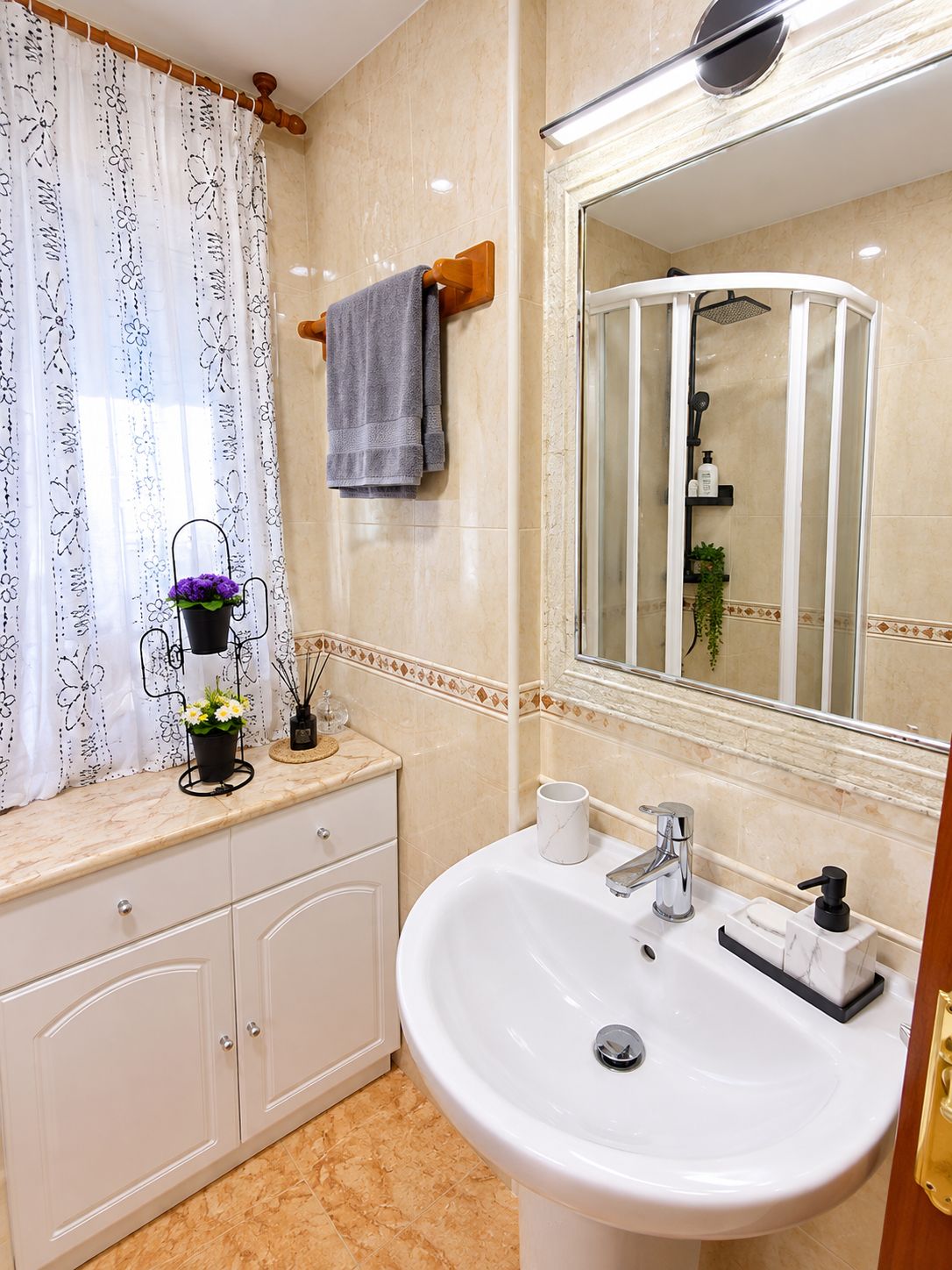 Un baño con lavamanos blanco, un espejo, toallero y zona de ducha.