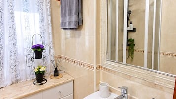 Un baño con lavamanos blanco, un espejo, toallero y zona de ducha.