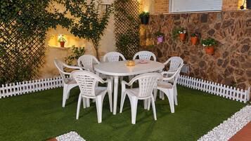 A patio with a round table and white chairs, surrounded by a white picket fence and a stone wall.