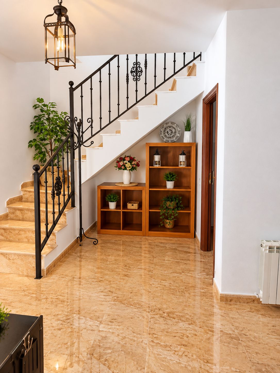 Una escalera con barandilla de metal negro, una consola de madera con plantas en macetas y un radiador blanco en el suelo.