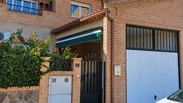 Una casa de ladrillo de dos pisos con una puerta de garaje blanca, una reja metálica y un automóvil blanco estacionado en la parte delantera.