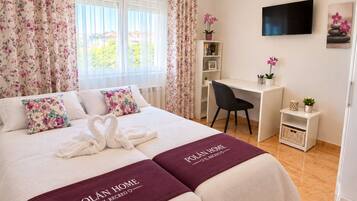 Habitación de hotel con cama, escritorio, silla, televisor y ventana con cortinas.