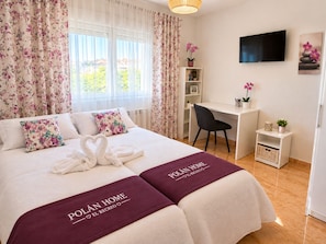 A hotel room with a bed, a desk, a chair, a TV, and a window with curtains.