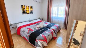 Una habitación de hotel con cama, mesita de noche, lámpara, aire acondicionado instalado en la pared y ventana con cortinas.