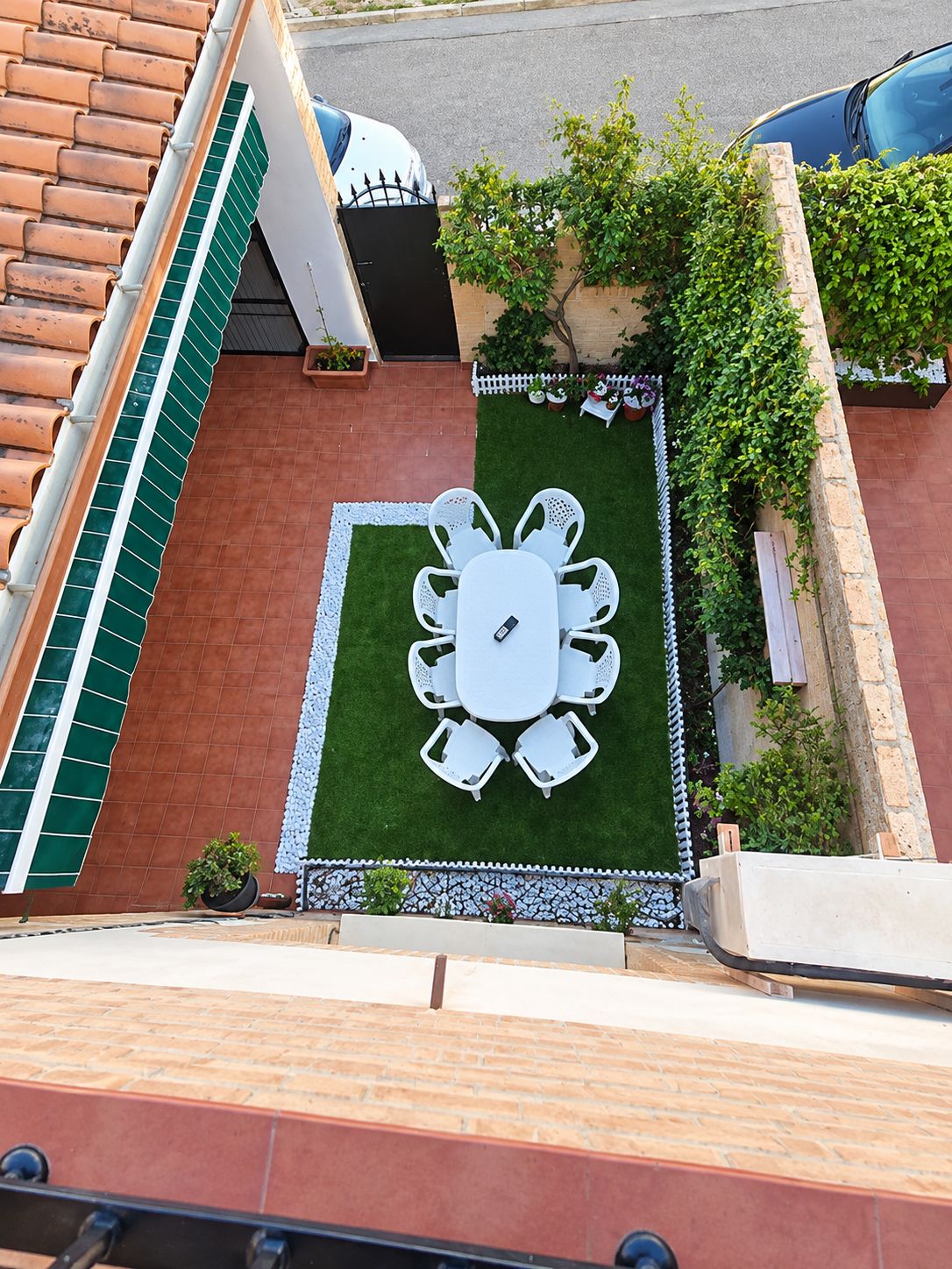 Una terraza en la azotea con una mesa y sillas blancas, rodeada por un pequeño jardín con una valla blanca y follaje.