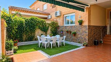 Un patio con una mesa y sillas blancas, rodeado por una cerca de piquetes blancos y un muro de piedra con plantas en macetas.