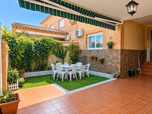 A patio with a white table and chairs, surrounded by a white picket fence, and a stone wall with potted plants.