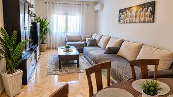 A living room with a sofa, TV, and decorative plants.
