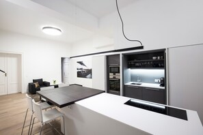 Et moderne køkken med en central ø, indbygget ovn og et spiseområde med barstole.