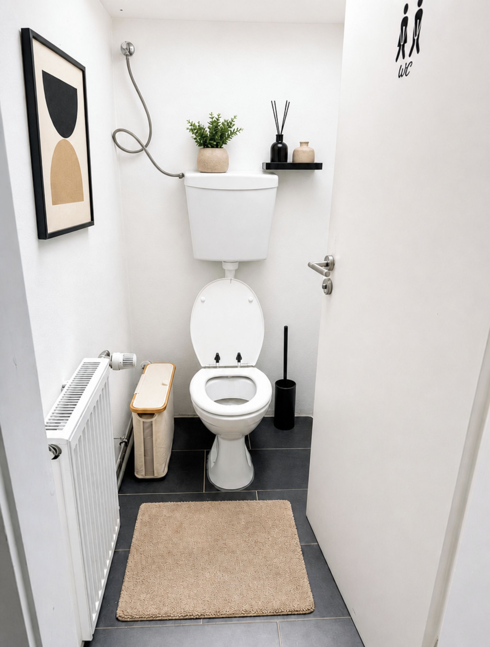 Een kleine, moderne badkamer met een wit toilet, een radiator, een beige vloerkleed, een potplant en een zwart schapje met een vaas en rietverdamper.