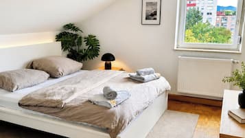 Une chambre à coucher avec un lit, une lampe de chevet, un radiateur, une fenêtre donnant sur un beau paysage et une plante.