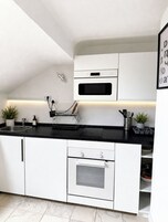 Una cocina moderna con armarios blancos, encimera negra, horno empotrado y microondas.
